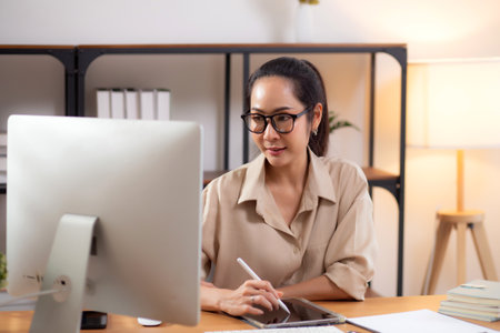 Happiness young businesswoman using desktop computer while writing on tablet on desk in living room at home office, business woman using computer, entrepreneur or freelance, business and commercial.の写真素材