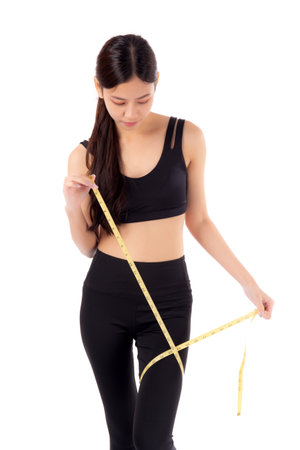 Portrait young asian woman in sportswear holding measuring tape leg for weight loss isolated white background, girl weightloss with workout and exercise while measurement with leg, sport and diet.の写真素材