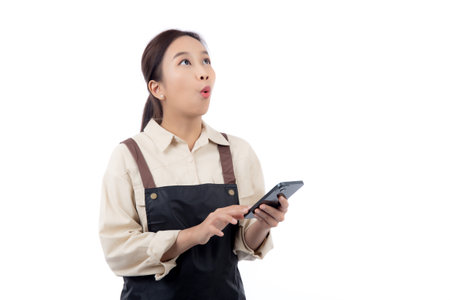 Portrait happy young asian barista woman in apron while looking smart phone gesture surprised isolated white background, waitress or entrepreneur watching smartphone, small business or startup.の写真素材