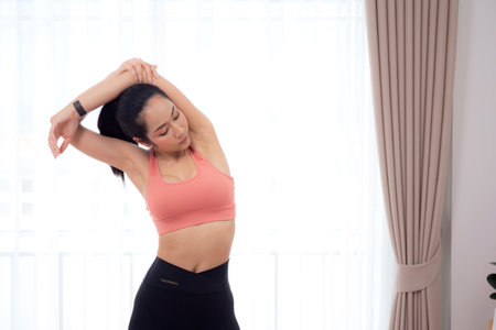 Beautiful young asian woman standing workout with warmup and stretch muscle arm and hands at home, female exercise for relax with sport, motivation and determined for health, sport concept.の写真素材