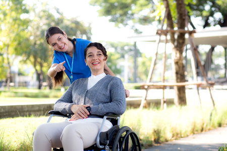 Young caucasian nurse care with patient while pushing wheelchair for relax and rehabilitation in park, caregiver support and assistance patient, medical and insurance, health and therapy.の写真素材