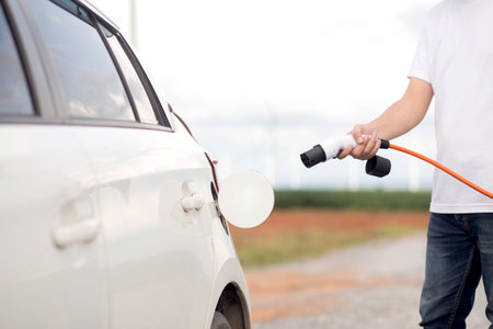 Closeup of hand of person plugging in an electric car for charging station outdoors, sustainable energy and modern transportation, electric vehicle and energy, innovation and recharge.の写真素材