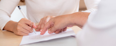 Closeup hand writing on paper for signature about insurance or agreement medical in modern medical office, contract or finance about medical, hand woman signing with doctor for treatment in hospital.の写真素材