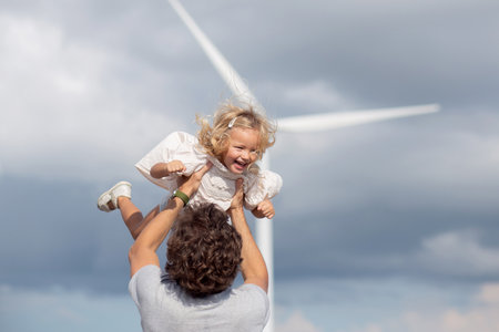 Family with father and daughter playful together with throwing on sky, renewable energy and family happiness, bonding and conservation of environment with sustainable, power energy and windmill.の写真素材