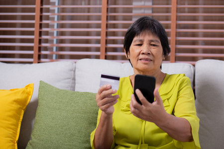 Senior asian woman sitting on sofa using smart phone shopping online with credit card buying to internet, female payment with business with smartphone, purchase and payment, business and finance.の写真素材