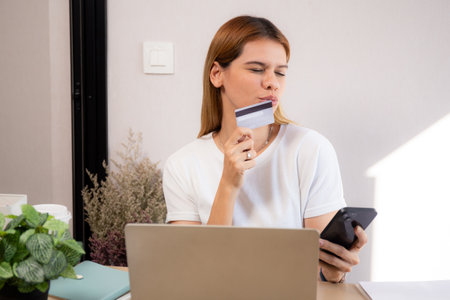 Happy young caucasian woman holding credit card or debit card paying with shopping online while on smartphone, woman with spending with transaction of finance, business and financial.の写真素材