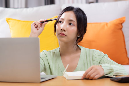 Young woman planning and strategy about finance and investment or tax while thoughtful in living room at home, woman with expense and budget while thinking of home, business and finance.の写真素材