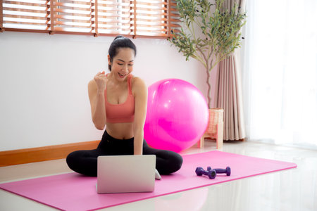 Young asian woman watch laptop for practice yoga and workout in living room at home, woman using chat bot on notebook with artificial intelligence with for training and exercise, sport and wellbeing.の写真素材