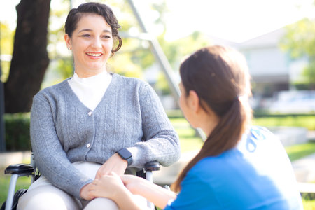 Young caucasian nurse comforting with patient while sitting on wheelchair in outdoor park, doctor woman support and counseling with patient, caregiver and service, medical and consoling.の写真素材