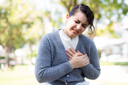 Caucasian woman chest pain in outdoor park, emergency of patient with injury, urgency and disease of woman, medical and accident, sick of patient and expression, medical and health, one person.の写真素材