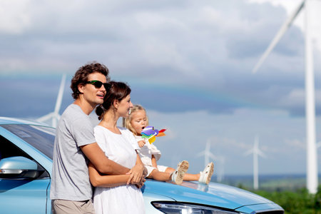 Happy family by a car with wind turbines, happiness family and bonding, recreation and renewable with innovation, windmill with resource sustainable power, travel in vacation and environmental.の写真素材