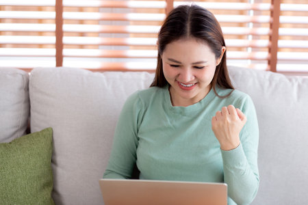 Young asian business woman working with laptop sitting on sofa in home office, businesswoman using on notebook in living room at home, woman relax with using laptop while success, business concept.の写真素材