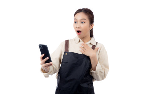 Portrait happy young asian barista woman in apron while looking smart phone gesture surprised isolated white background, waitress or entrepreneur watching smartphone, small business or startup.の写真素材