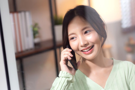 Young asian businesswoman telephone smiling and relax in living room at home office, cheerful woman standing talking with smart phone in home, expression and emotion, business and communication.の写真素材