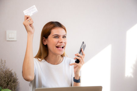 Happy young caucasian woman holding credit card or debit card paying with shopping online while laughing on smartphone, woman with spending with transaction of finance, business and financial.の写真素材