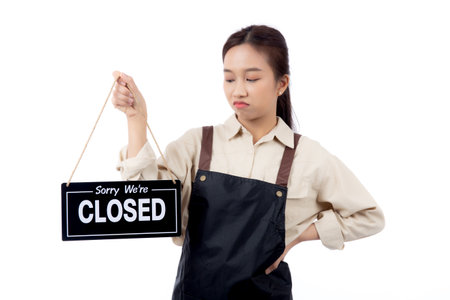 Portrait young asian barista woman wearing apron holding closed sign with unhappiness, waitress woman holding signboard with closed, startup business and entrepreneur with bankruptcy.の写真素材