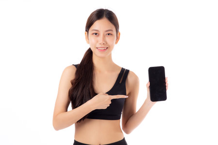 Young asian woman in sportswear workout holding and presenting blank screen smartphone isolated white background, girl in sportswear showing mockup smart phone, sport and health care concept.の写真素材