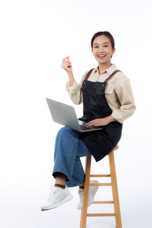 Portrait young asian business woman wearing apron holding laptop computer isolated white background, waitress or barista holding laptop computer with confident, cut out, business or freelance.の写真素材