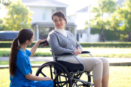 Young caucasian nurse comforting with patient while sitting on wheelchair in outdoor park, doctor woman support and counseling with patient, caregiver and service with senior, medical and consoling.の写真素材