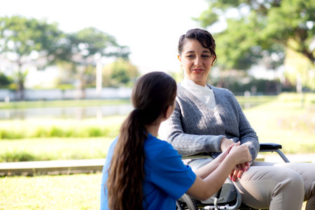 Young caucasian nurse comforting with patient while sitting on wheelchair in outdoor park, doctor woman support and counseling with patient, caregiver and service, medical and consoling.の写真素材