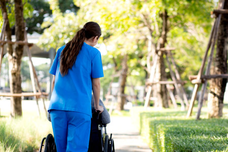 Young caucasian nurse care with patient while pushing wheelchair for relax and rehabilitation in park, caregiver support and assistance patient, medical and insurance, health and therapy.の写真素材