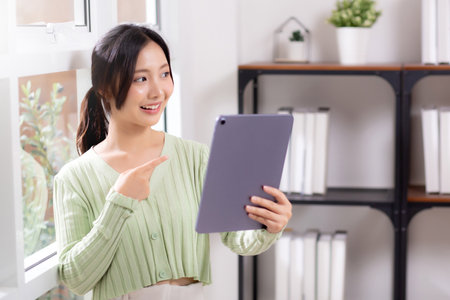 Portrait young asian business woman using digital tablet computer for video call by the window in living room at home office, businesswoman and expression while video call, lifestyle and business.の写真素材