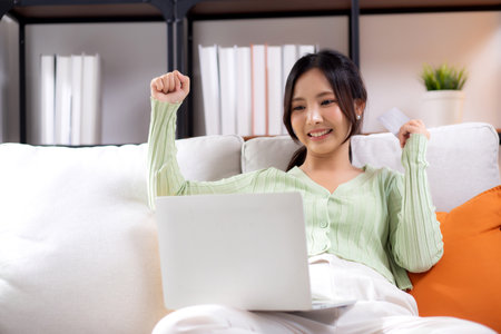 Young asian woman sitting on sofa using laptop computer shopping online with credit card buying to internet while cheerful, female payment with business, purchase and payment, business and finance.の写真素材
