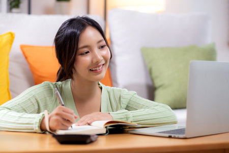 Young asian woman planning and strategy about finance and investment or tax while writing on textbook in living room at home, woman with expense and budget of home, business and finance.の写真素材