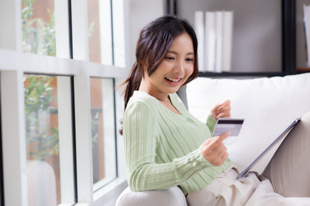 Young asian woman sitting on sofa using tablet computer shopping online with credit card buying to internet while cheerful, female payment with business, purchase and payment, business and finance.の写真素材