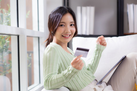 Young asian woman sitting on sofa using tablet computer shopping online with credit card buying to internet while cheerful, female payment with business, purchase and payment, business and finance.の写真素材