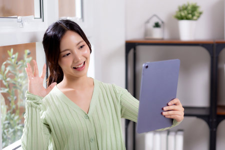 Portrait young asian business woman using digital tablet computer for video call by the window in living room at home office, businesswoman and expression while video call, lifestyle and business.の写真素材