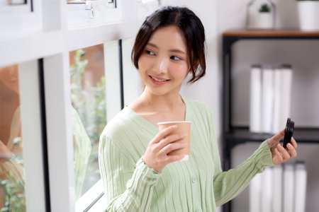 Portrait young asian woman relax and enjoyment with drinking coffee by the window in living room at home, woman smiling with happiness and comfortable drinking beverage at home, lifestyle and leisure.の写真素材