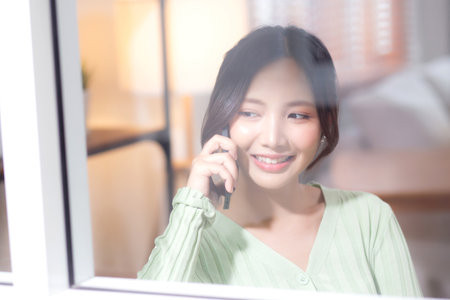 Young asian businesswoman telephone smiling and relax in living room at home office, cheerful woman standing talking with smart phone in home, expression and emotion, business and communication.の写真素材