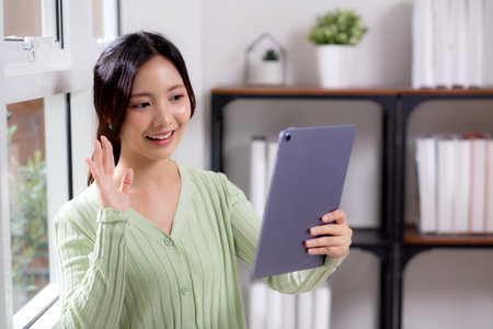 Portrait young asian business woman using digital tablet computer for video call by the window in living room at home office, businesswoman and expression while video call, lifestyle and business.の写真素材