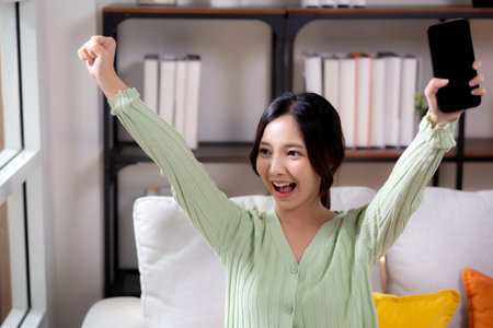Young asian businesswoman looking smartphone smiling and relax sitting on sofa in living room at home, cheerful woman watching smart phone sitting on couch in home, lifestyle and communication.の写真素材