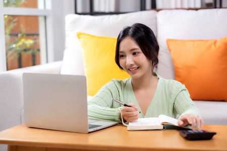 Young asian woman planning and strategy about finance and investment or tax while writing on textbook in living room at home, woman with expense and budget of home, business and finance.の写真素材