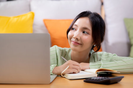 Young asian woman planning and strategy about finance and investment or tax while writing on textbook in living room at home, woman with expense and budget of home, business and finance.の写真素材