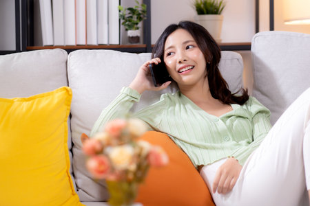 Young asian businesswoman telephone smiling and relax sitting on sofa in living room at home, cheerful woman talking with smart phone sitting on couch in home, lifestyle and communication.の写真素材