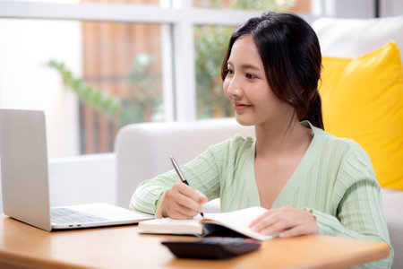 Young asian woman planning and strategy about finance and investment or tax while writing on textbook in living room at home, woman with expense and budget of home, business and finance.の写真素材