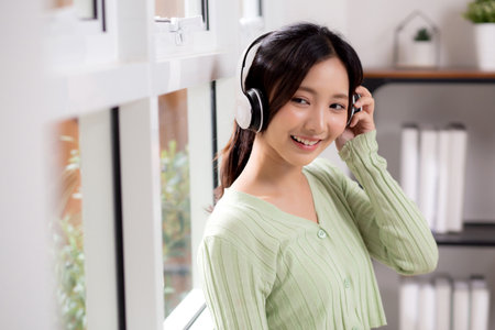 Portrait happy young woman wearing headphones listening music while standing with fun and enjoy in the living room at home, happiness female with entertainment, one person, lifestyle concept.の写真素材