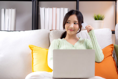 Young asian woman sitting on sofa using laptop computer shopping online with credit card buying to internet while thoughtful, female payment with business, purchase and payment, business and finance.の写真素材