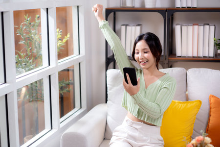 Young asian businesswoman looking smartphone smiling and relax sitting on sofa in living room at home, cheerful woman watching smart phone sitting on couch in home, lifestyle and communication.の写真素材