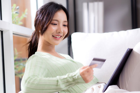 Young asian woman sitting on sofa using tablet computer shopping online with credit card buying to internet while cheerful, female payment with business, purchase and payment, business and finance.の写真素材