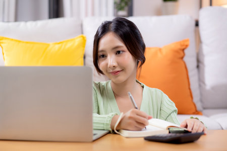 Young asian woman planning and strategy about finance and investment or tax while writing on textbook in living room at home, woman with expense and budget of home, business and finance.の写真素材
