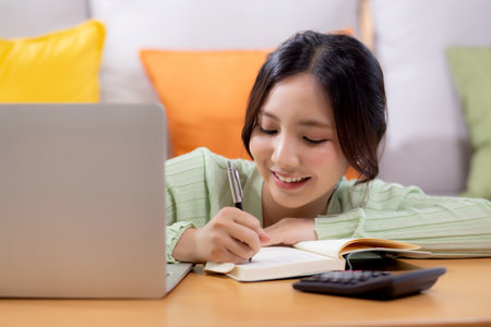 Young asian woman planning and strategy about finance and investment or tax while writing on textbook in living room at home, woman with expense and budget of home, business and finance.の写真素材