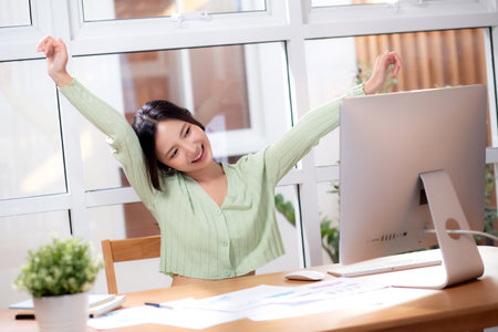 Young asian business woman using desktop computer for success in modern home office, businesswoman working with desktop computer while winning and satisfied in living room at home, business concept.の写真素材