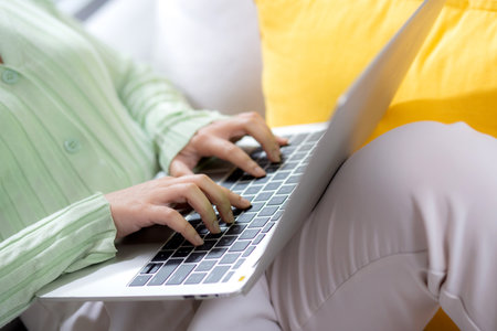 Closeup hands young woman sitting on sofa using laptop computer working from home in the living room at home, female is freelance using notebook online, one person, business and lifestyles concept.の写真素材