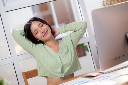 Portrait young asian businesswoman taking a break after overworked with stretching arm and hand in living room at home office, business woman relax with ergonomic, business and health.の写真素材