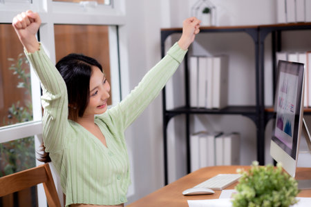 Young asian business woman using desktop computer for success in modern home office, businesswoman working with desktop computer while winning and satisfied in living room at home, business concept.の写真素材