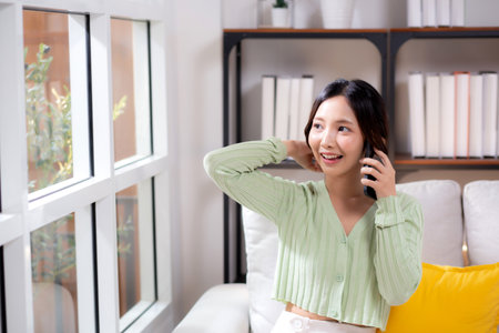 Young asian businesswoman telephone smiling and relax sitting on sofa in living room at home, cheerful woman talking with smart phone sitting on couch in home, lifestyle and communication.の写真素材